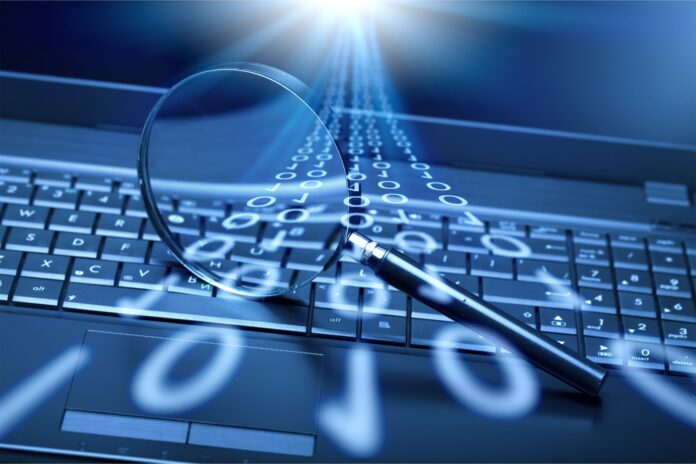 Laptop keyboard with binary scroll overlay underneath magnifying glass